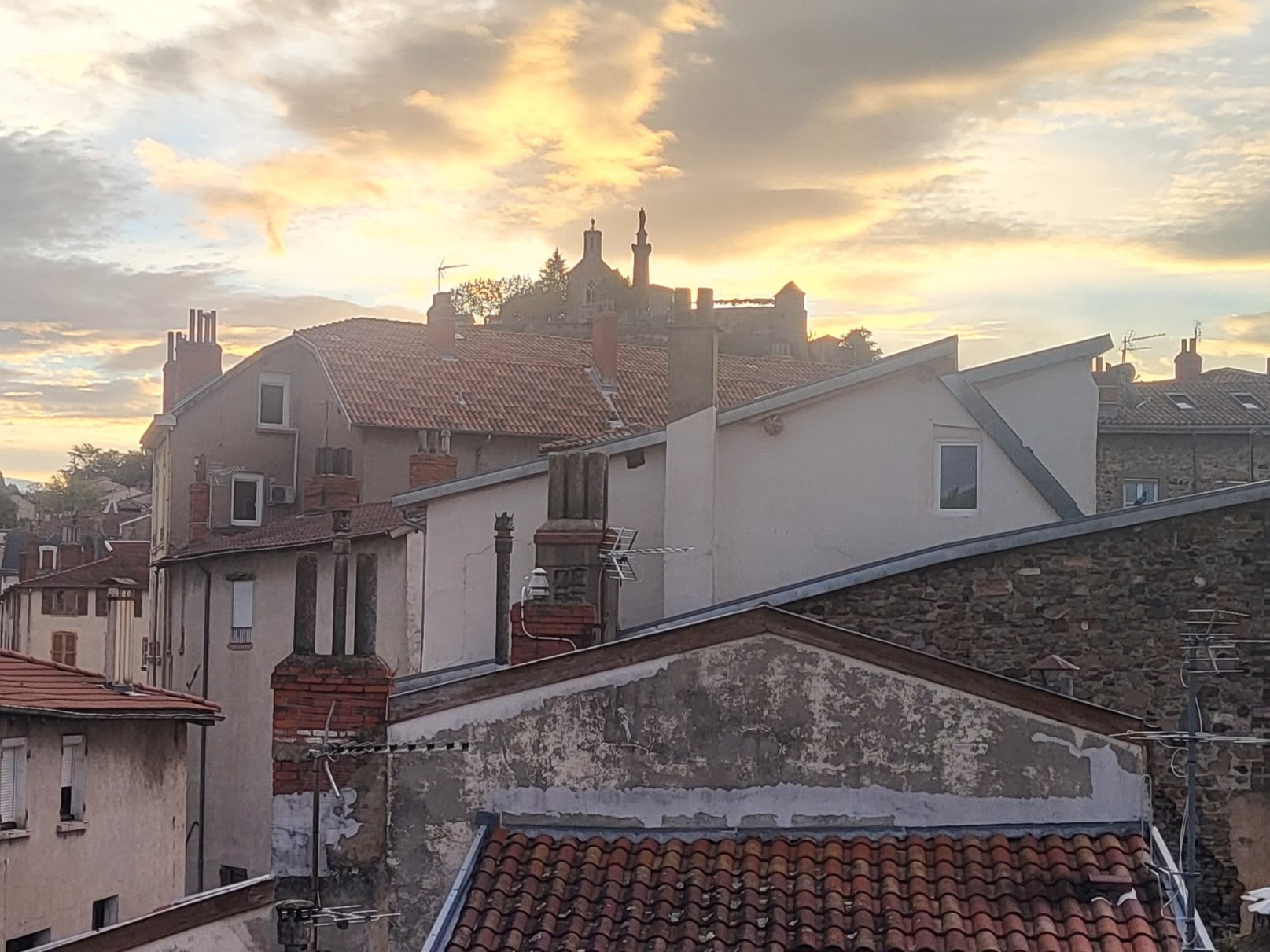 Toits et cheminées des maisons anciennes de Vienne, en Isère, au coucher du soleil. Vue sur la colline de Pipet avec sa chapelle