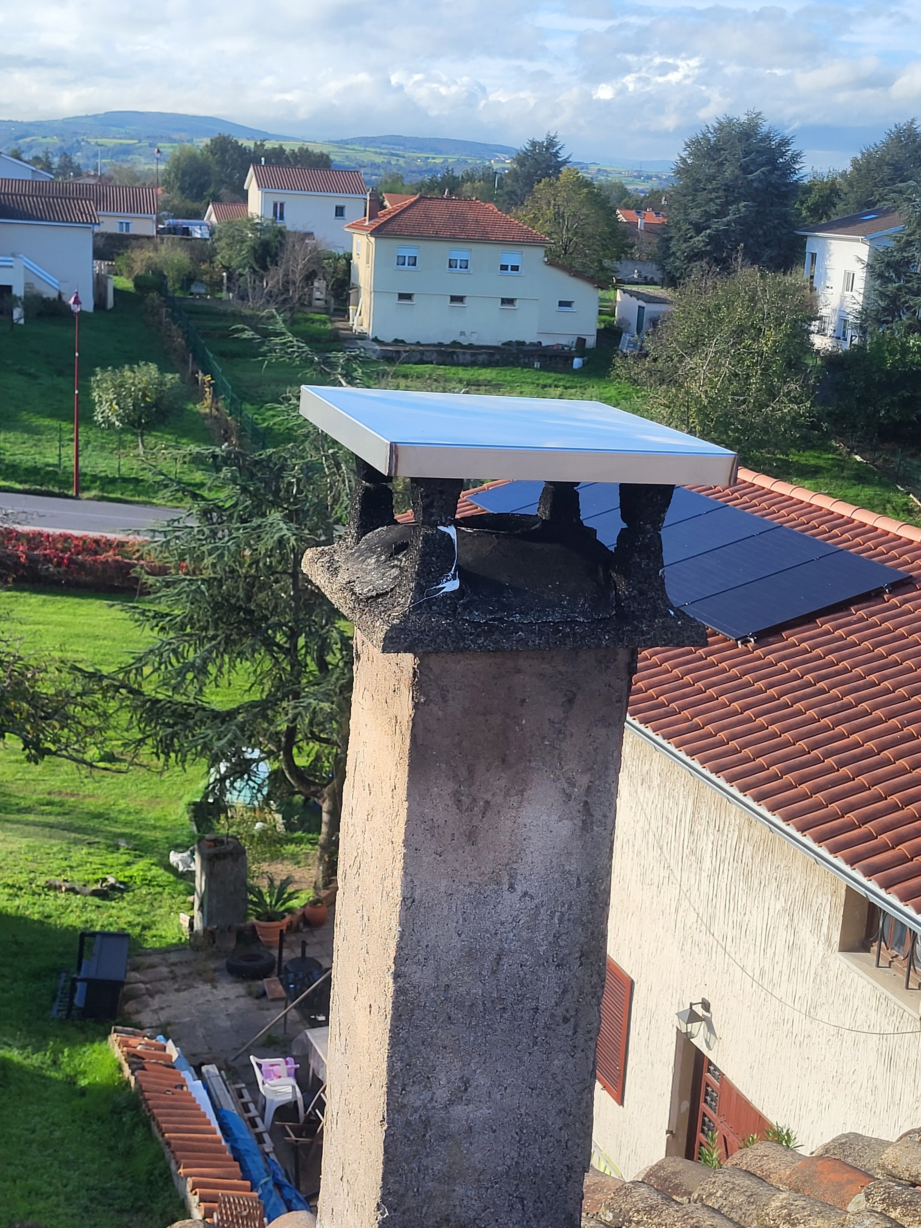 Cheminée en béton avec nouveau chapeau métallique installé par un ramoneur professionnel à Vienne pour éviter les infiltrations d'eau. Vue sur un quartier résidentiel avec toits en tuiles