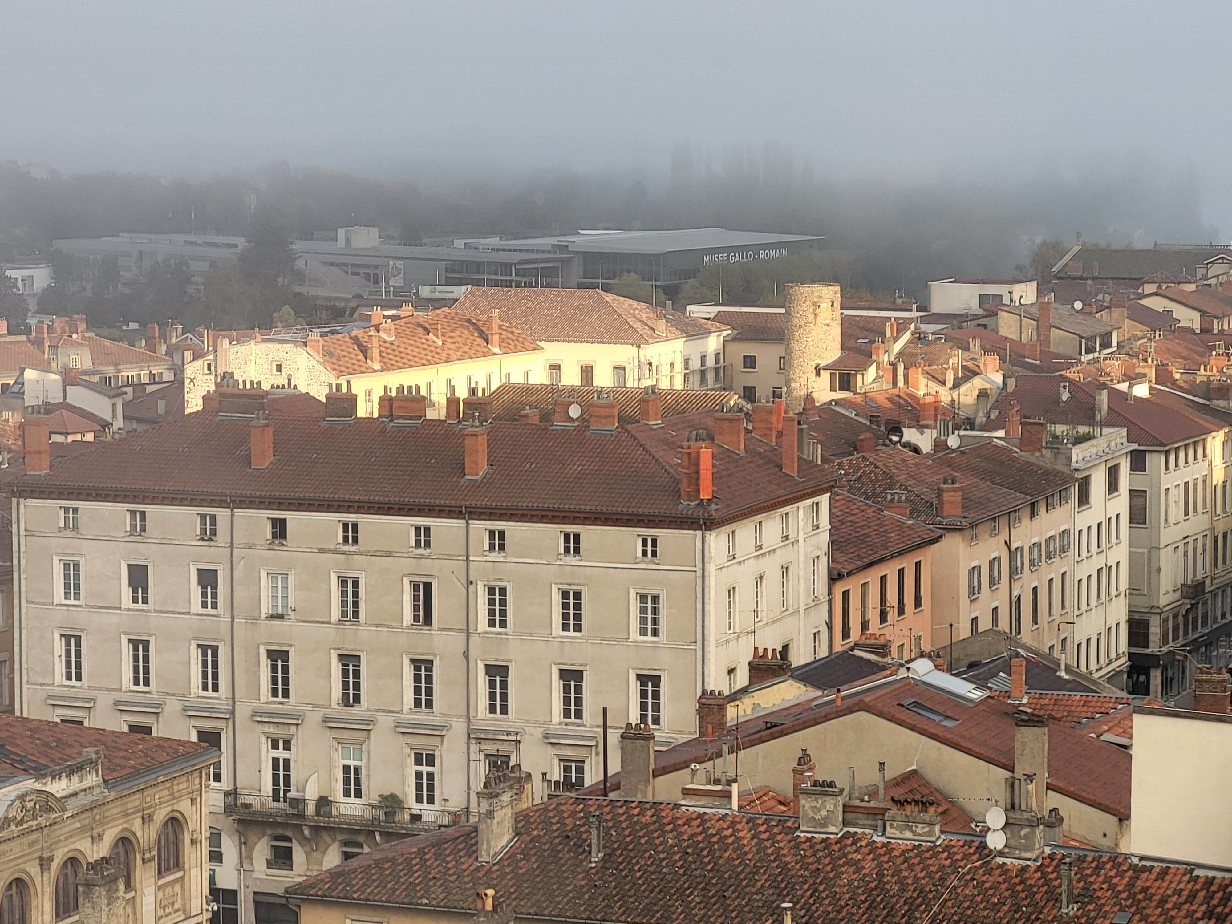 Vue sur les toits et cheminées du centre-ville de Vienne avec le Musée Gallo-Romain de Saint-Romain-en-Gal visible dans la brume matinale en arrière-plan